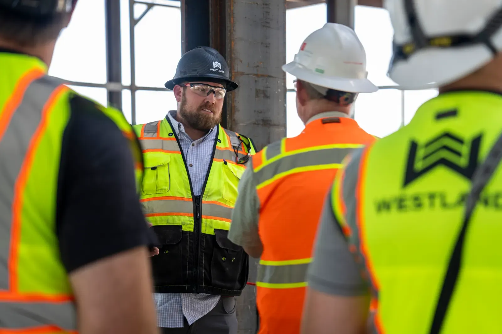 A Westland team member in a hard hat and safety vest talking with a group inside a building under construction