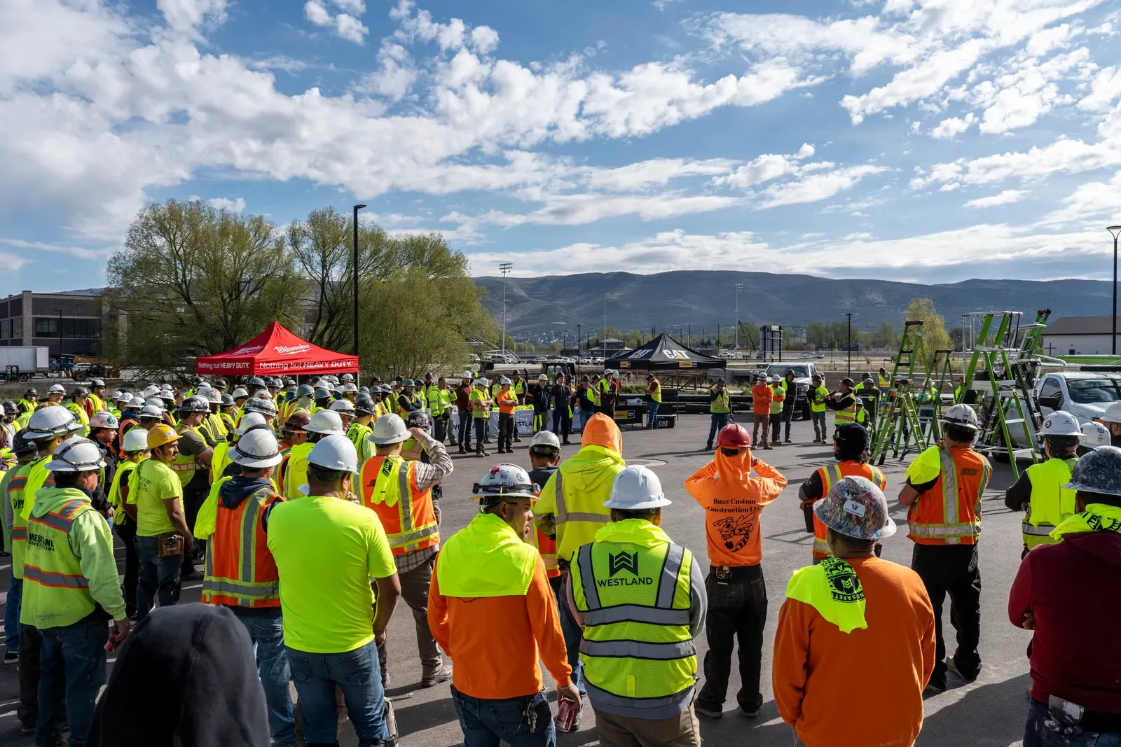 A large crowd of workers in hard hats and high-visibility vests gathered outdoors for a safety event
