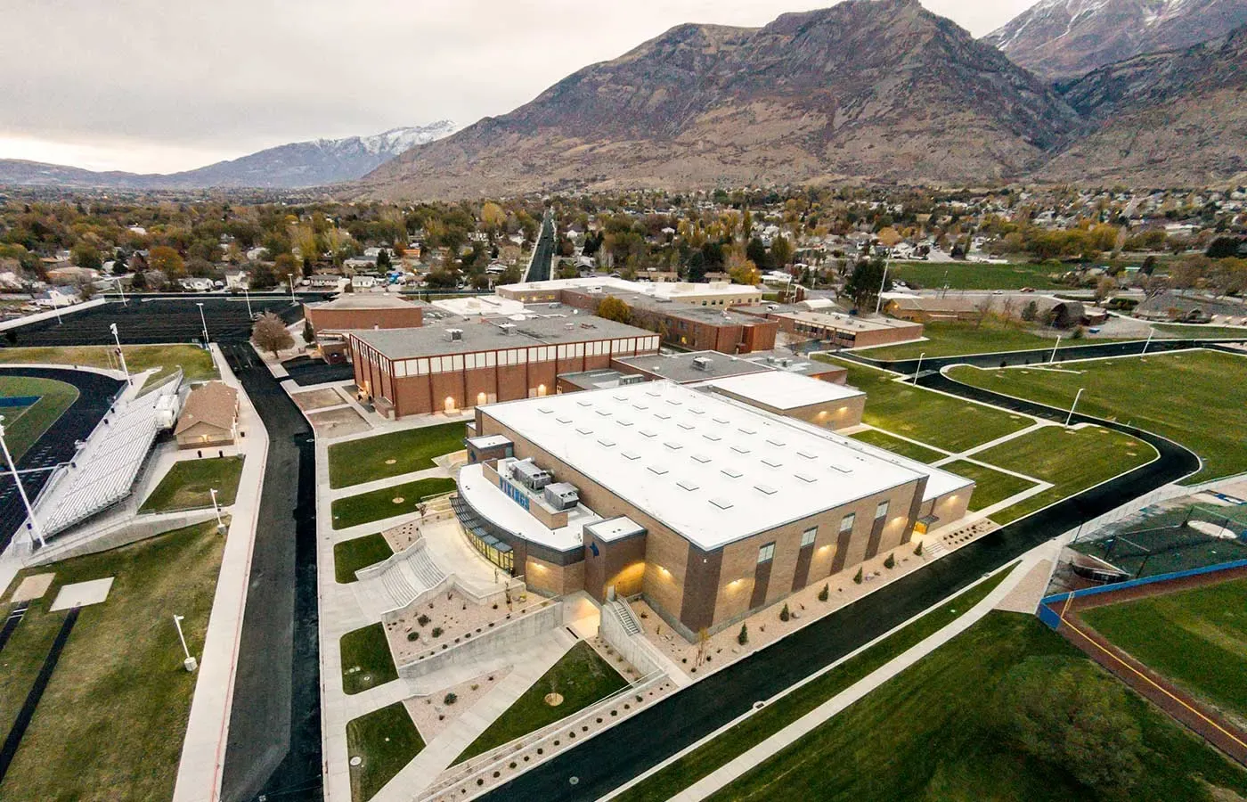 Aerial view of the field house and school campus with athletic fields and mountains behind.