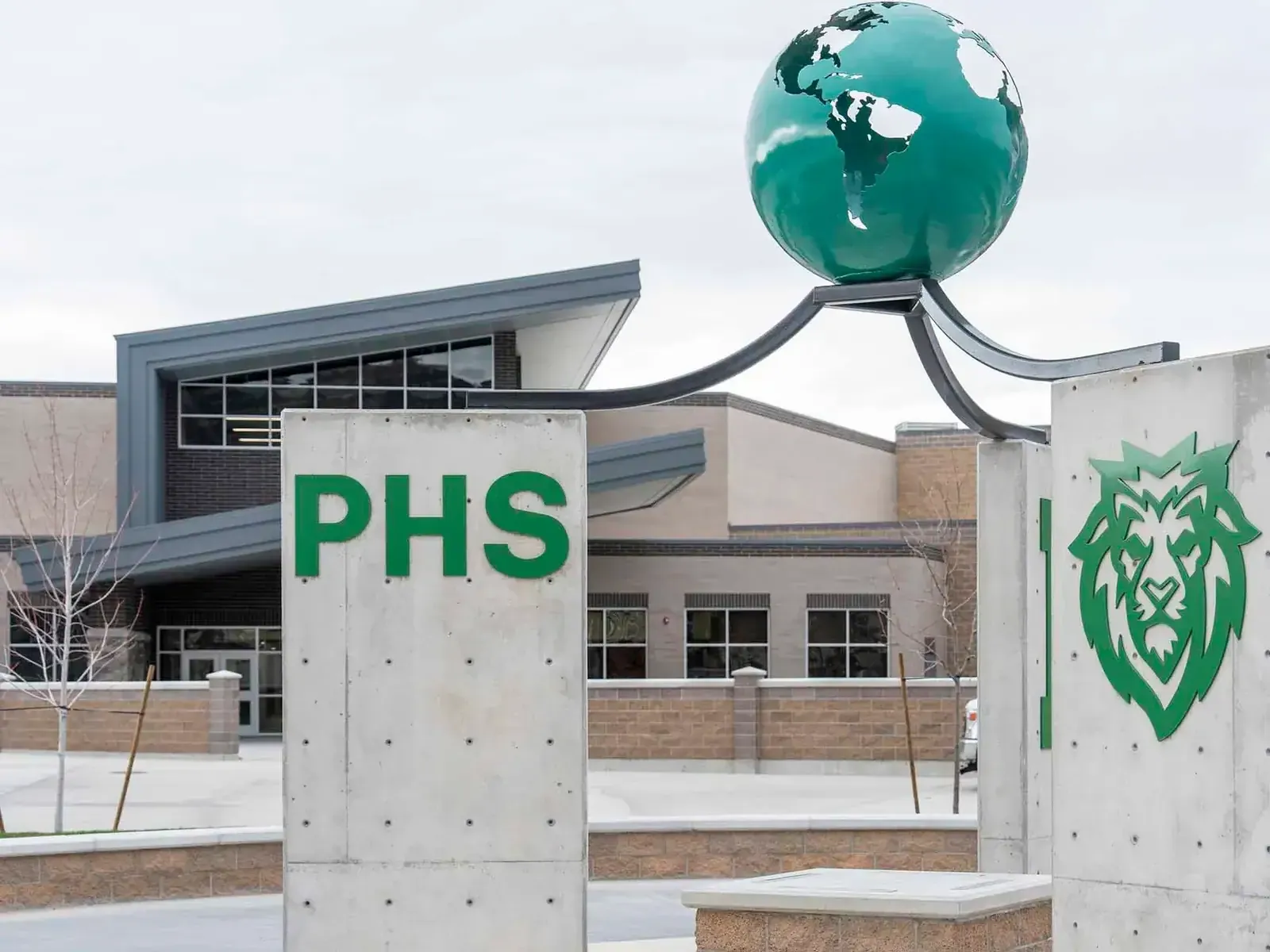 Entrance plaza with a green PHS sign, a lion emblem and a globe sculpture in front of the school building