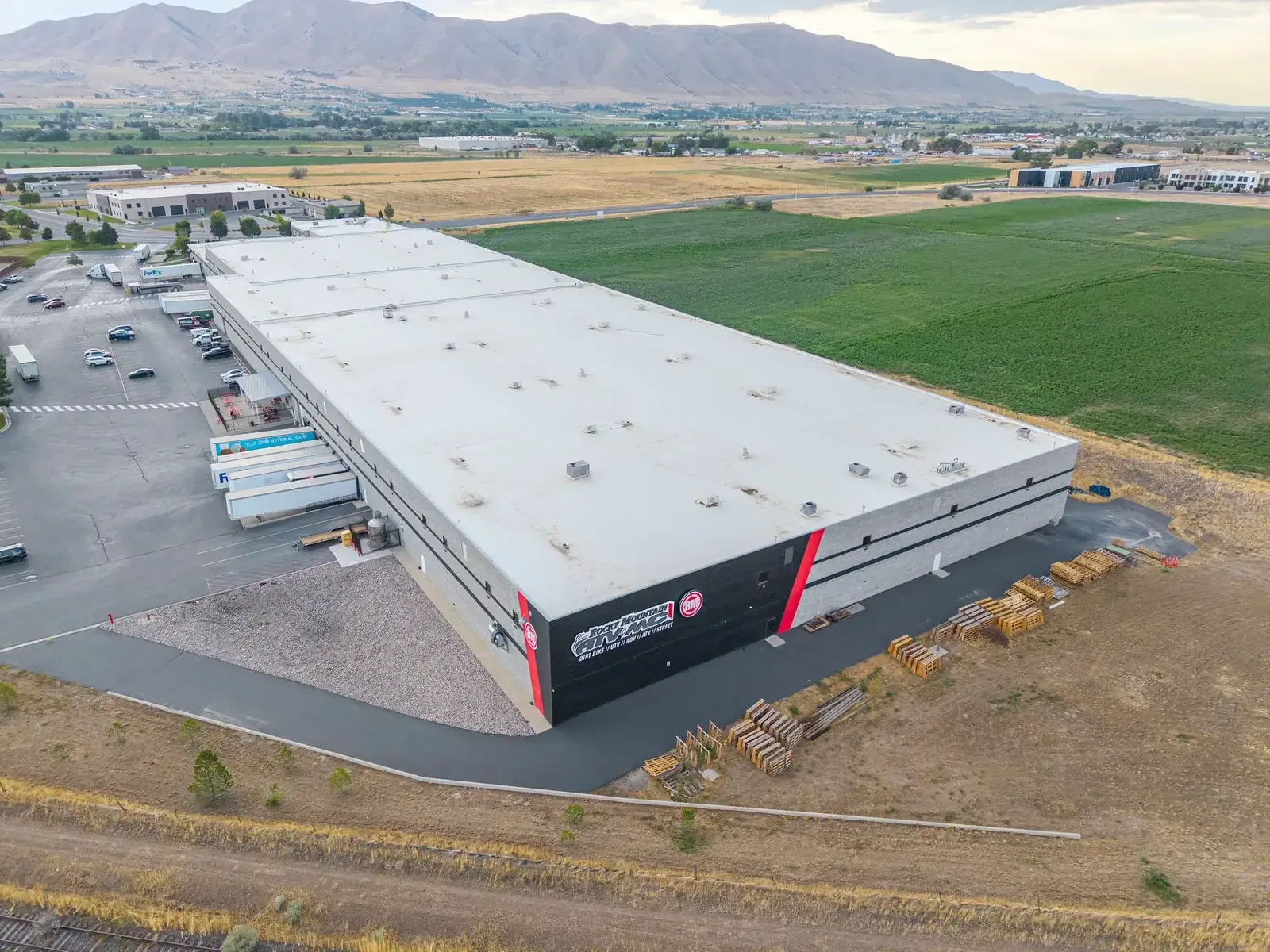Angled aerial view of the warehouse roof with truck docks on one side and farm fields beyond.