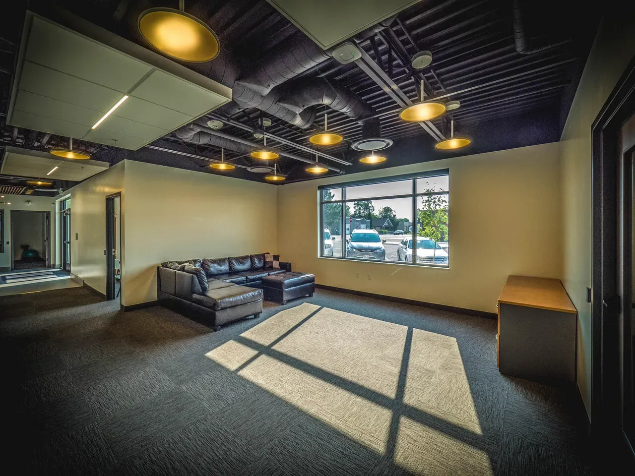 Lounge with a black leather sectional, round pendant lights, and exposed ceiling ductwork