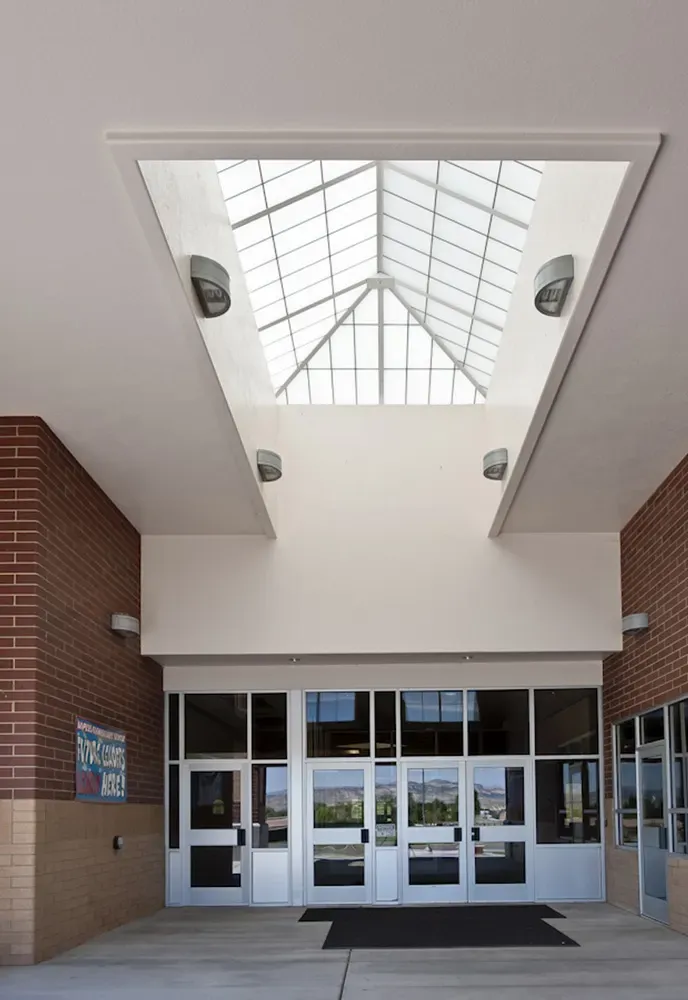 Covered school entry with a large skylight above a row of glass doors and brick walls on either side.