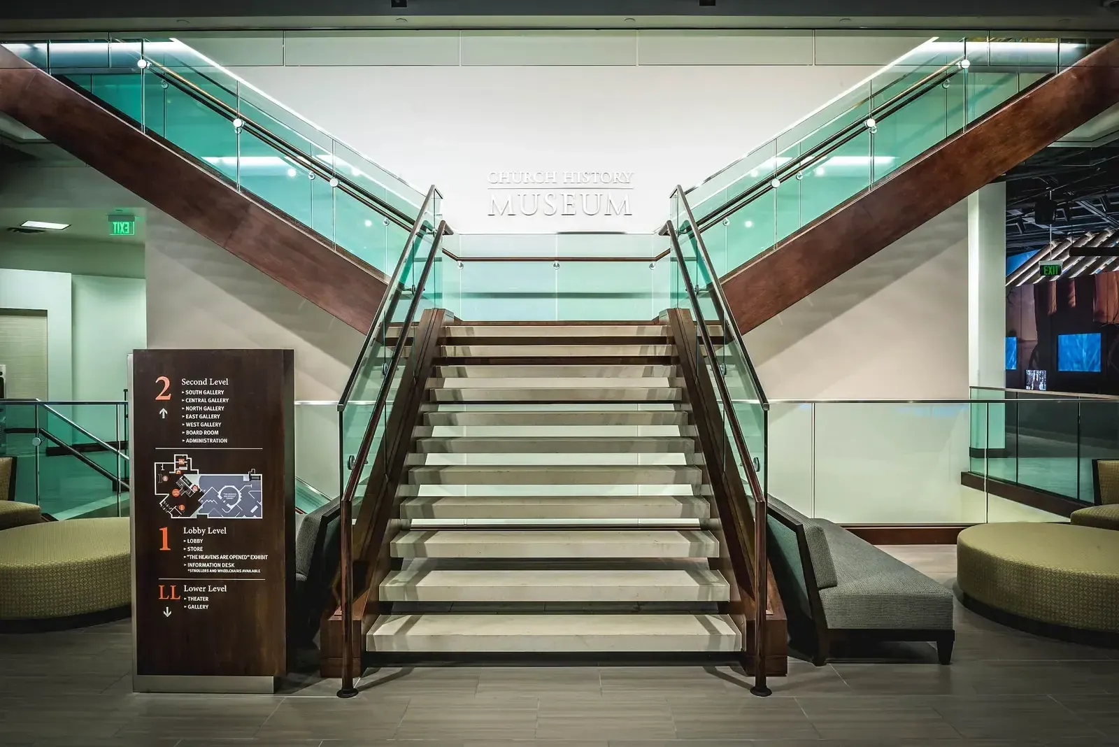 Grand staircase with glass railings and wood-trimmed handrails, with a level directory sign at the left