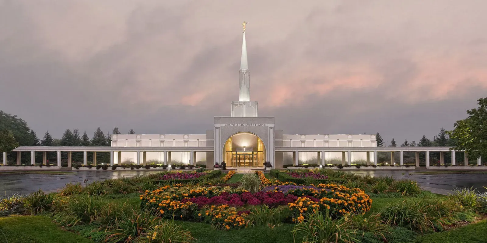 The illuminated temple at dusk with flower beds in the foreground and a pink-tinged sky behind