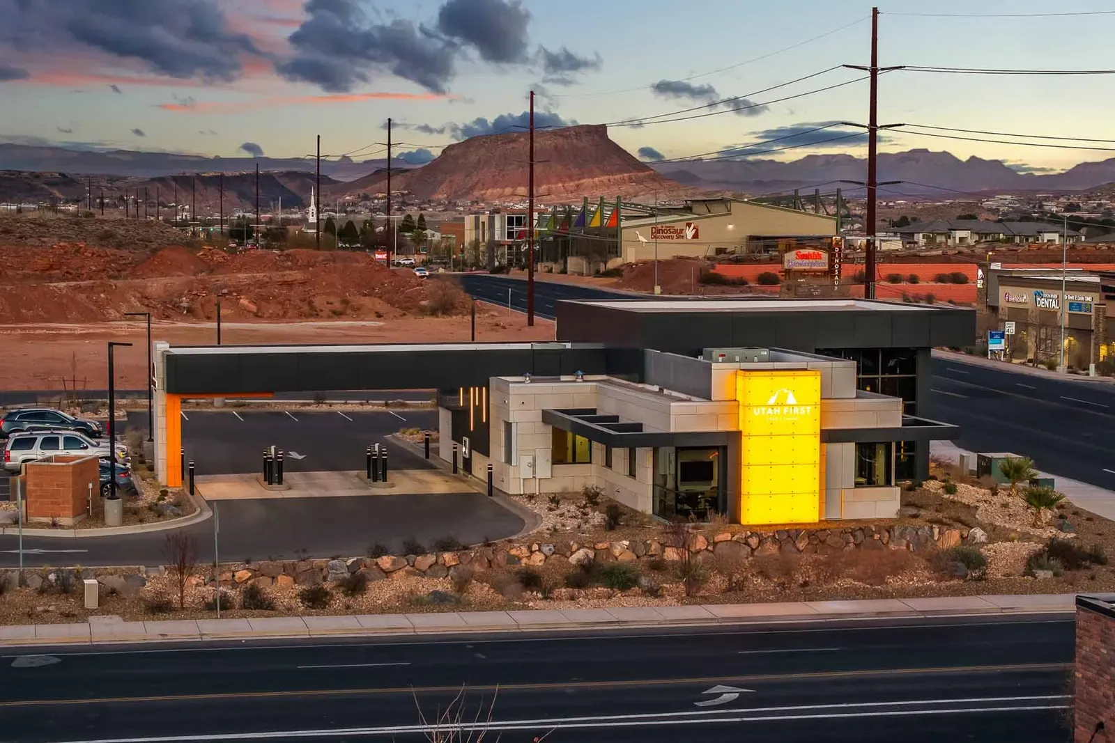 Dusk view of the branch and its drive-up canopy beside the road, with red rock hills in the distance.