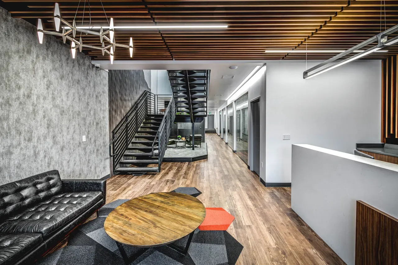 Open lobby with a leather sofa, a round wood table, a steel stair and a wood-slat ceiling