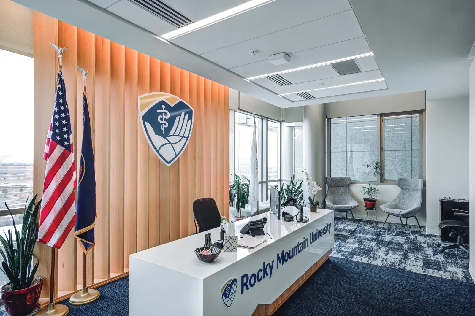 Reception desk with the Rocky Mountain University logo and flags in front of a wall of orange wood slats.