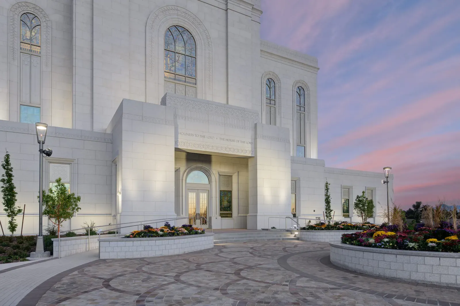 Temple entrance at dusk with a stone portico, a paved plaza, and curved planter walls.