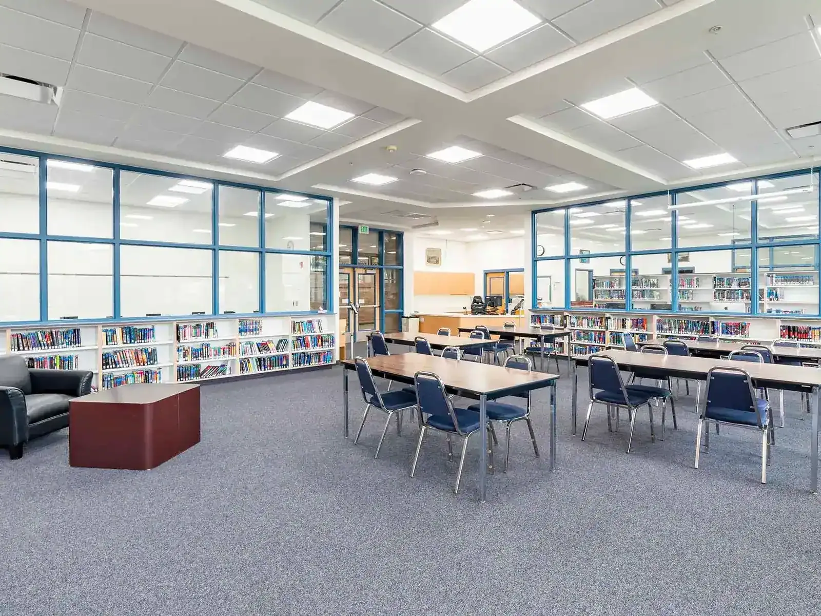 Library with blue-framed windows, low bookshelves, and long reading tables