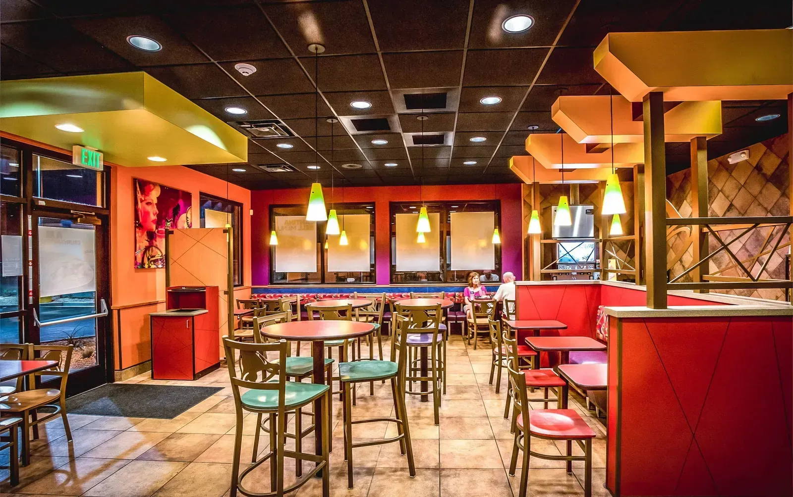 Dining room with red booths, green barstools, round tables and pendant lights
