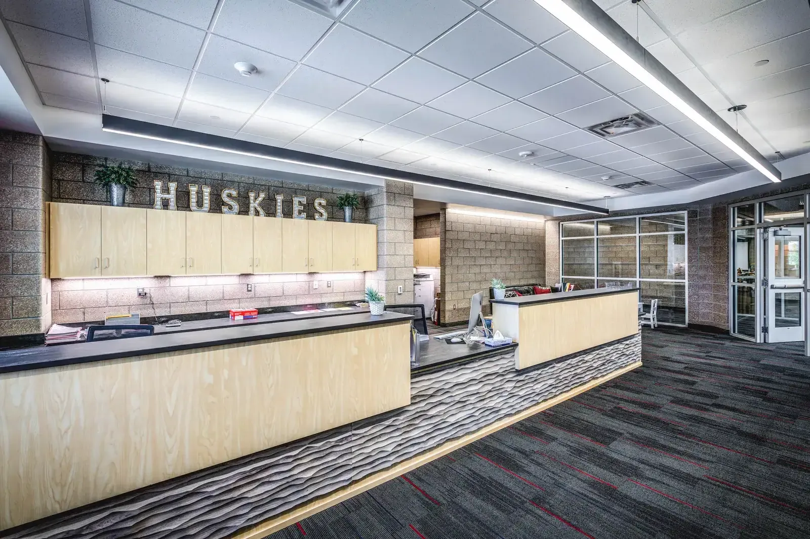 Main office reception counter under a HUSKIES sign, with light wood panels and a wavy gray counter facing