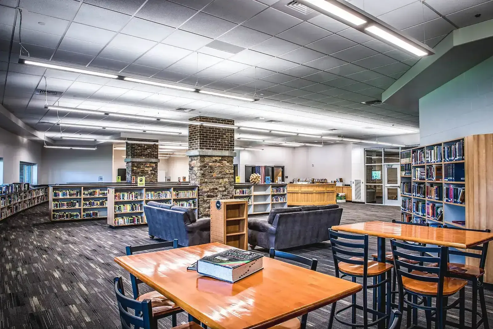 Library with bookshelves, stone-clad columns, tables and soft seating.