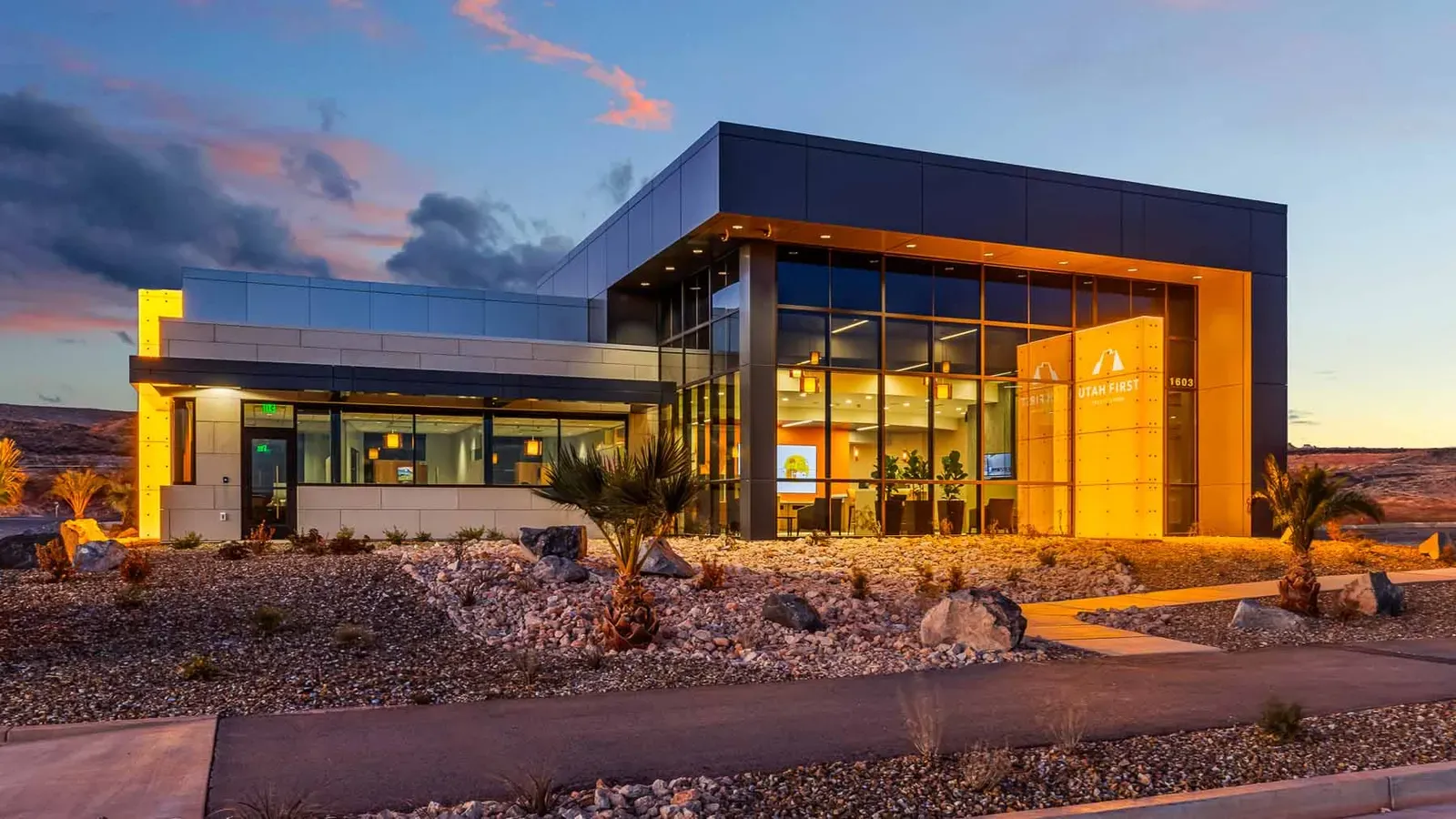 Branch building at dusk with glass walls, a glowing orange panel, and desert landscaping.
