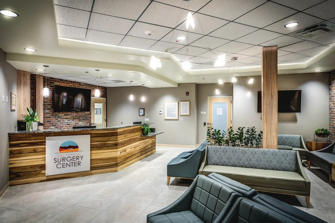 Surgery center lobby with a wood-slat reception desk, a brick accent wall, and upholstered waiting chairs.