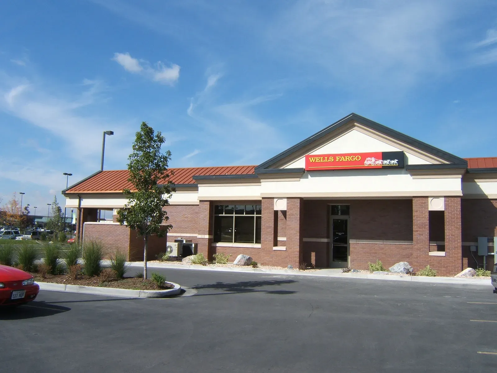Front of the Wells Fargo branch with a gabled entry, brick walls and a red metal roof.