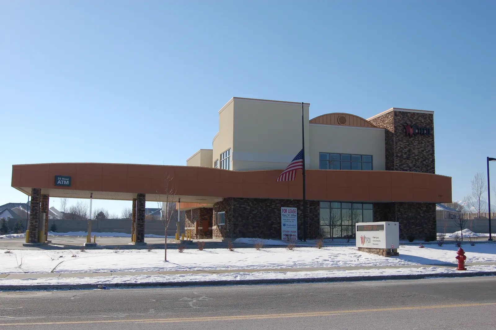 Two-story branch with stone and tan walls, a curved canopy over the drive-up lane and an ATM, seen with snow on the ground.