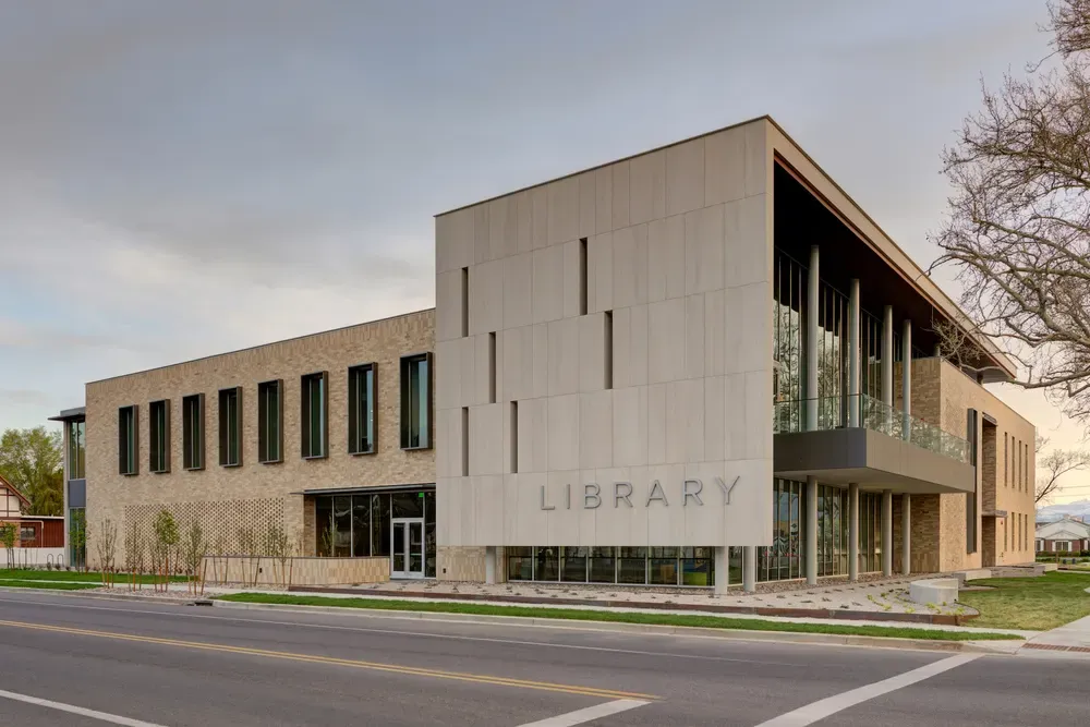 Street corner view of the building with the word LIBRARY on a tall paneled bay beside a brick wing with narrow windows