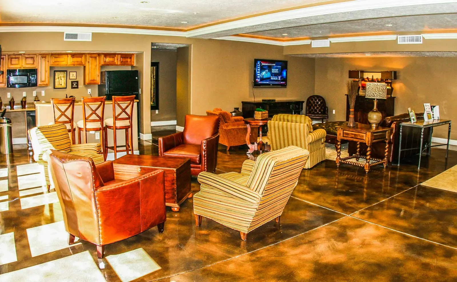 Clubhouse lounge with leather and striped armchairs, a wall-mounted television and a kitchen bar
