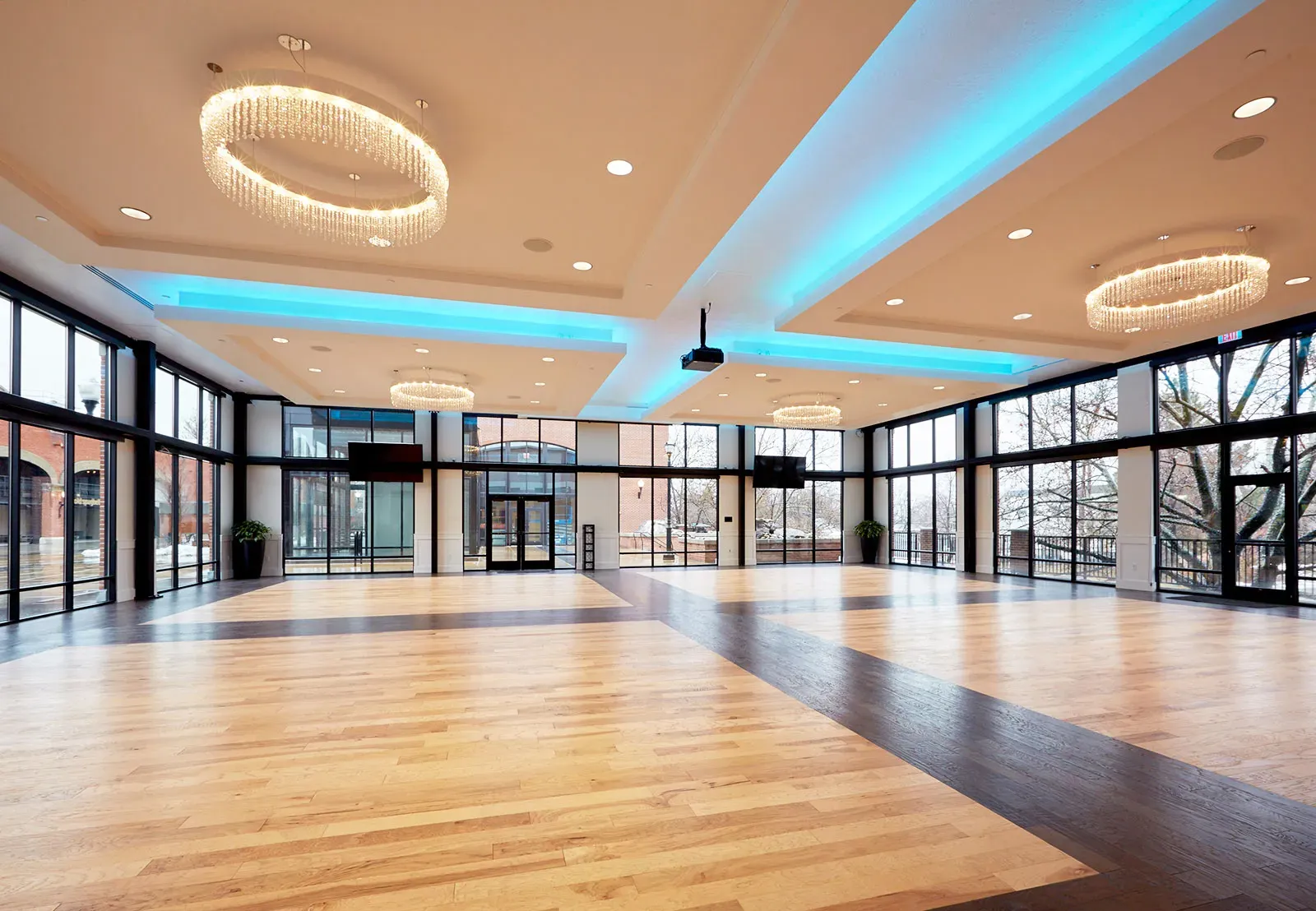 Event hall with a wood floor, glass walls, round crystal-style chandeliers and blue lighting along the ceiling coves.