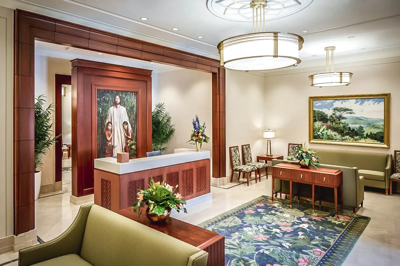 Temple reception area with a wood-framed desk, a painting of Christ with two children, a patterned rug, and upholstered chairs.