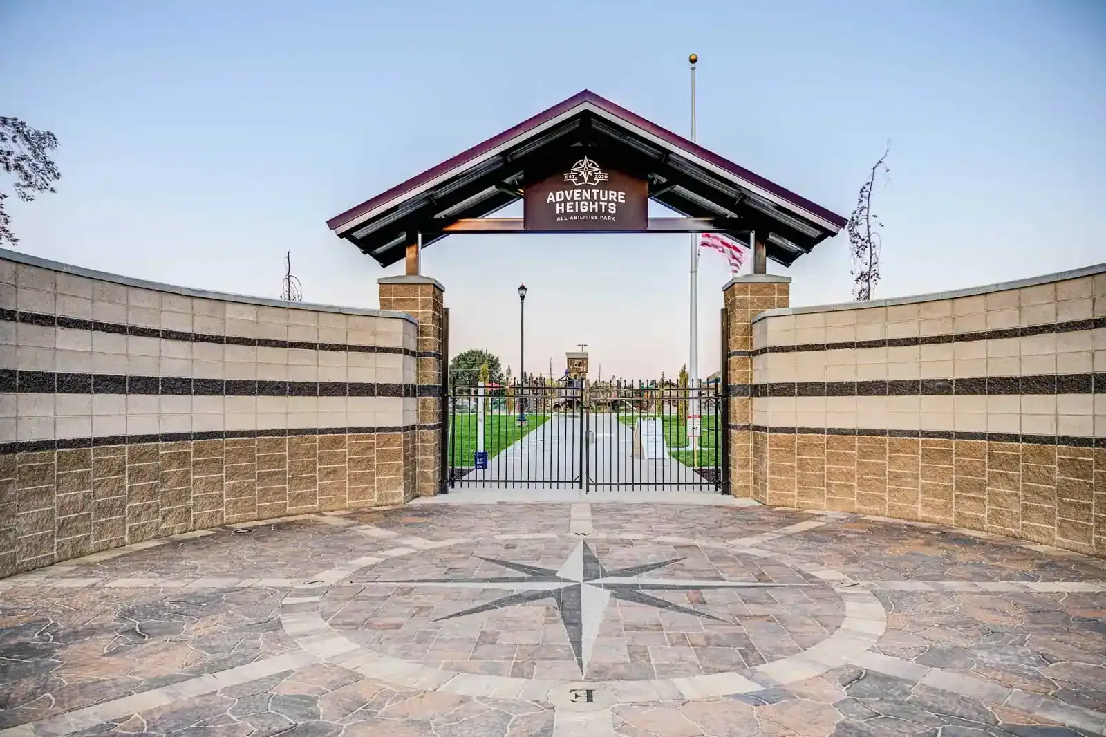 Park entrance gate under a timber canopy sign reading Adventure Heights, with stone-veneer walls and a compass rose in the paving