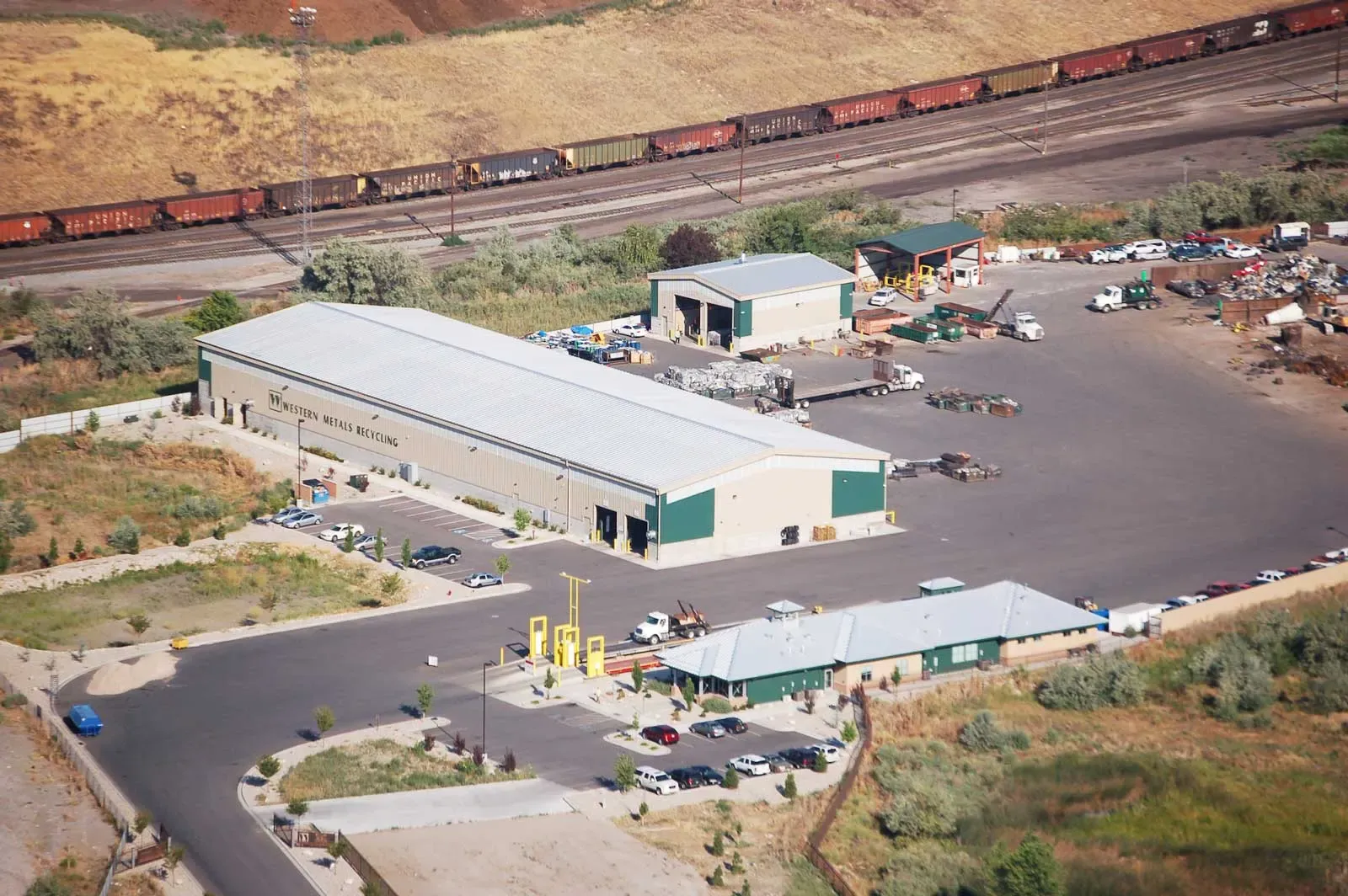 Aerial view of the recycling facility with a main building, smaller buildings and a rail line behind.