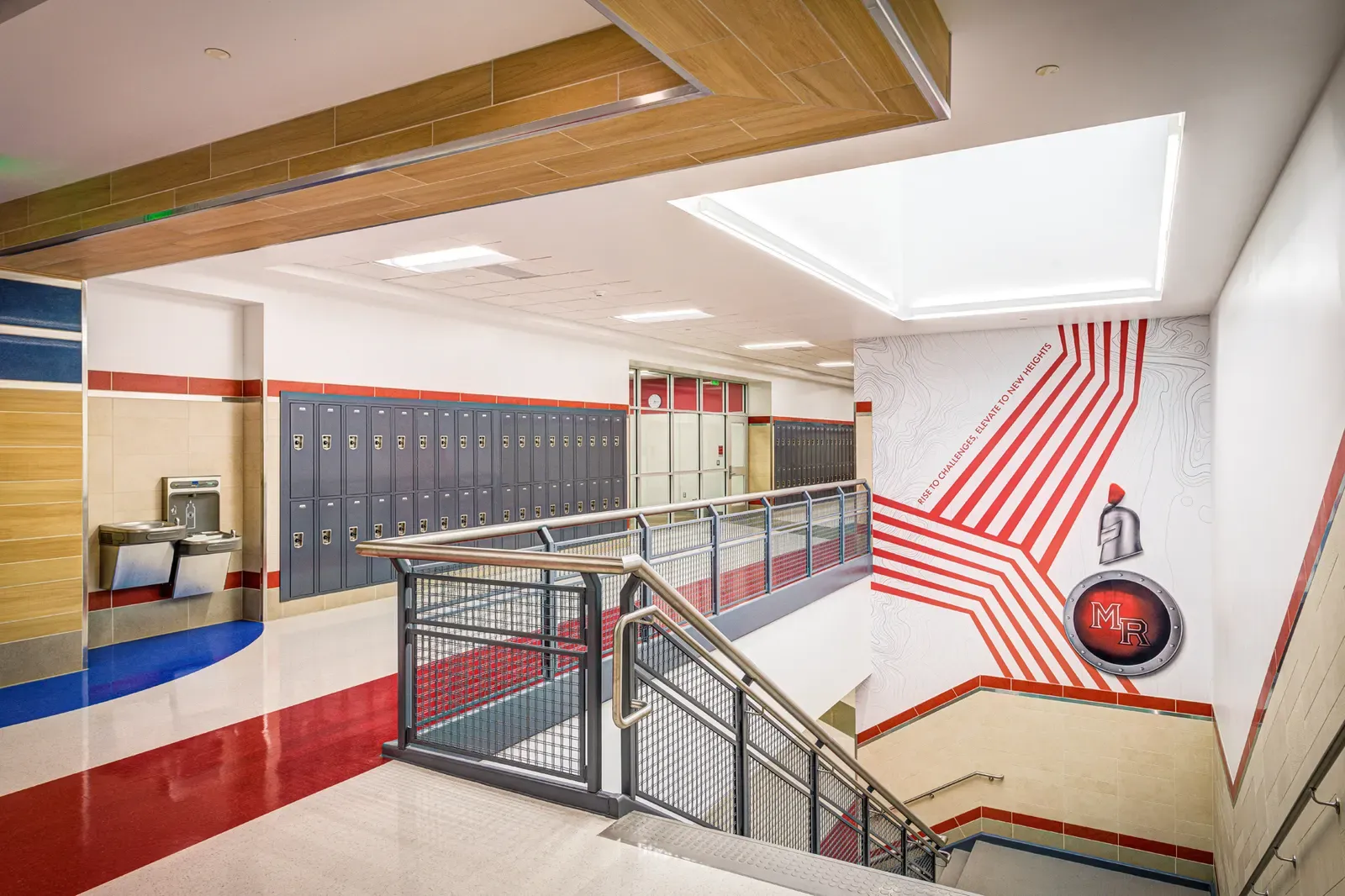 Hallway with lockers, red and white flooring, a staircase and a wall graphic.