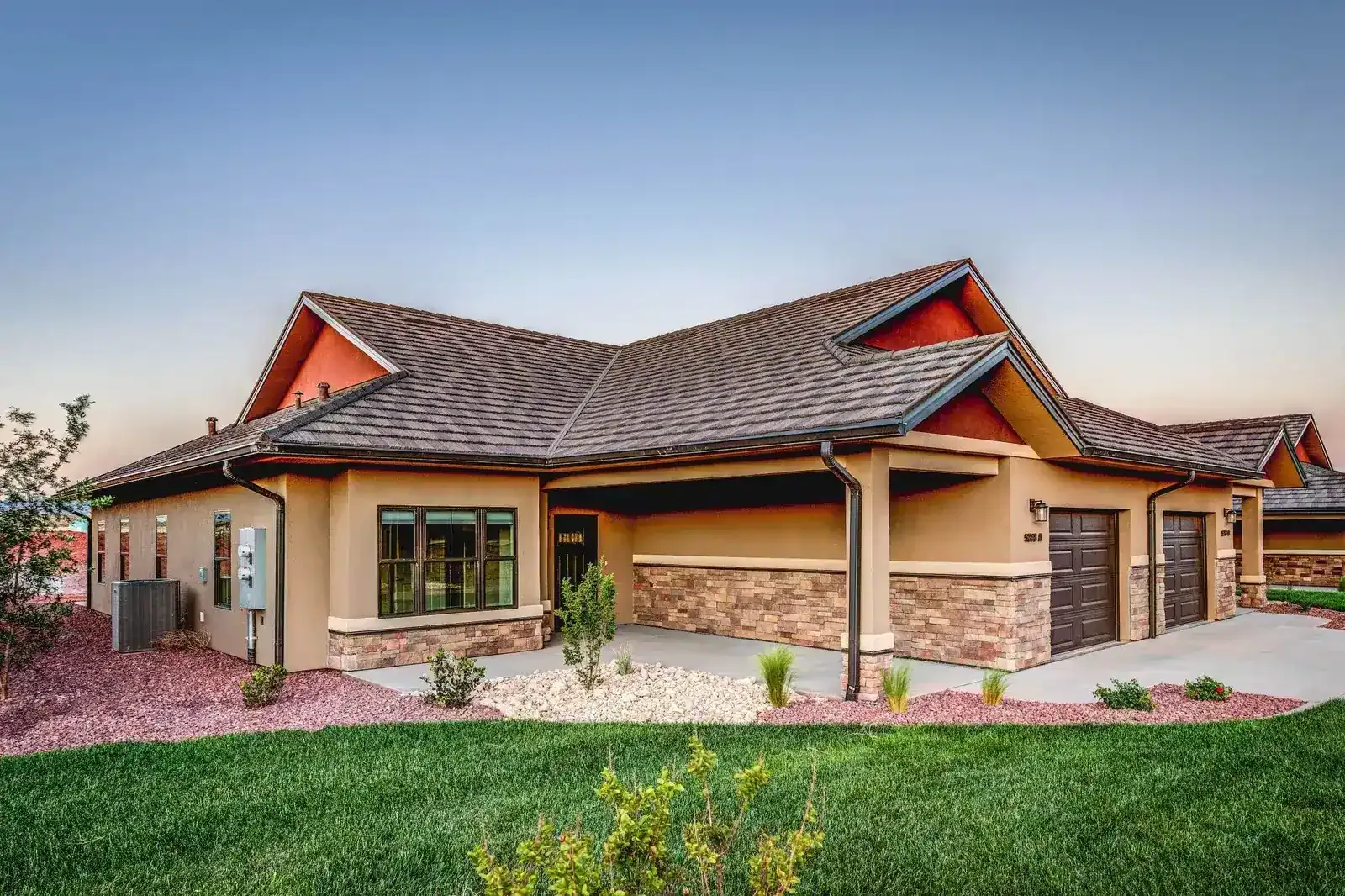 Single-story home with a stone-trimmed two-car garage and a low-pitched roof at dusk.