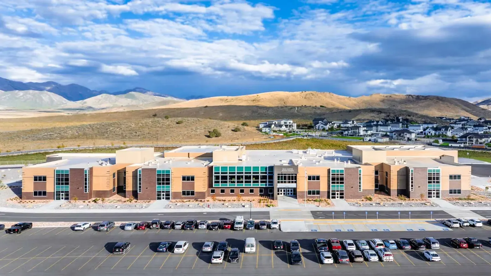Aerial view of the school's long brick building and parking lot with hills behind.