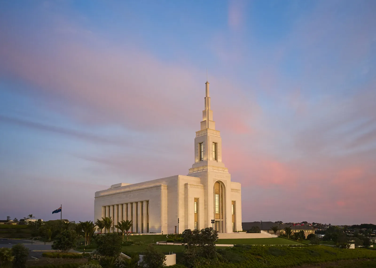 The temple and its spire at dusk under pink and blue clouds, with a flag on a pole to the left