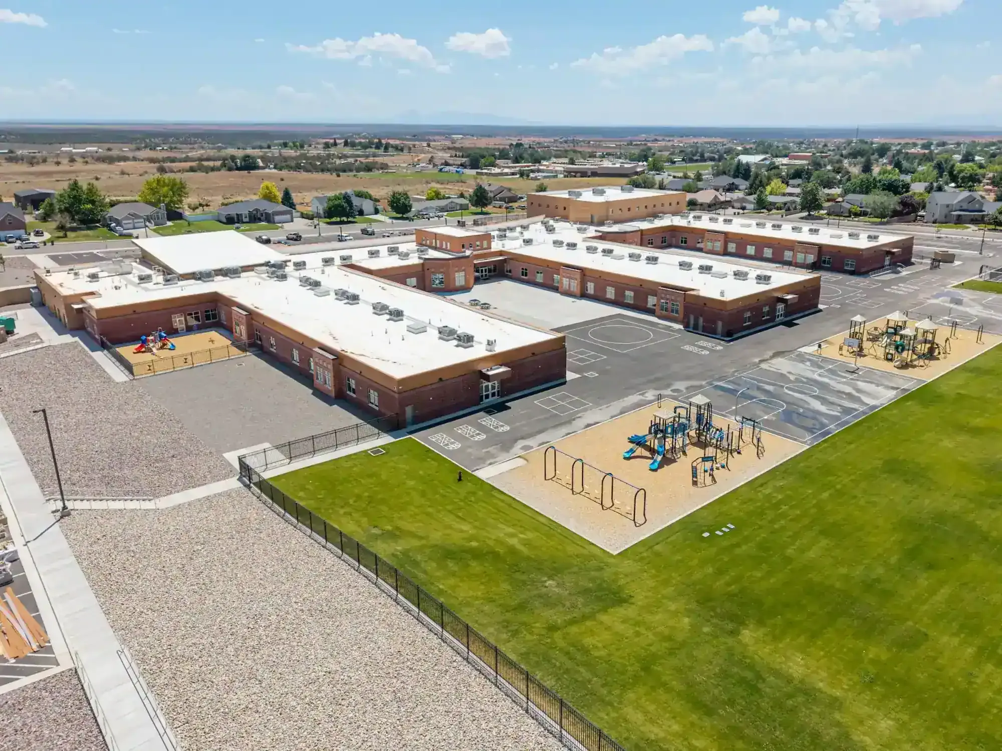 Aerial view of the new brick school with its playgrounds, paved play courts and green field.