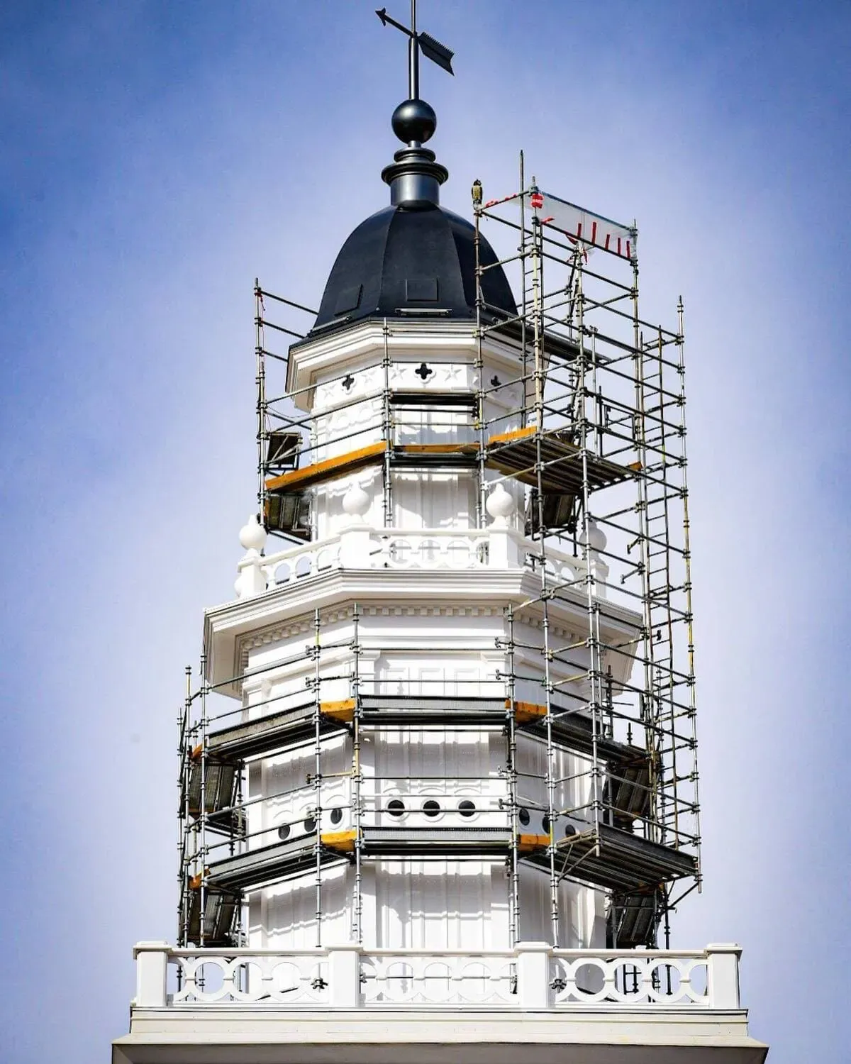 Temple tower during renovation, wrapped in scaffolding below a dark dome and weather vane.