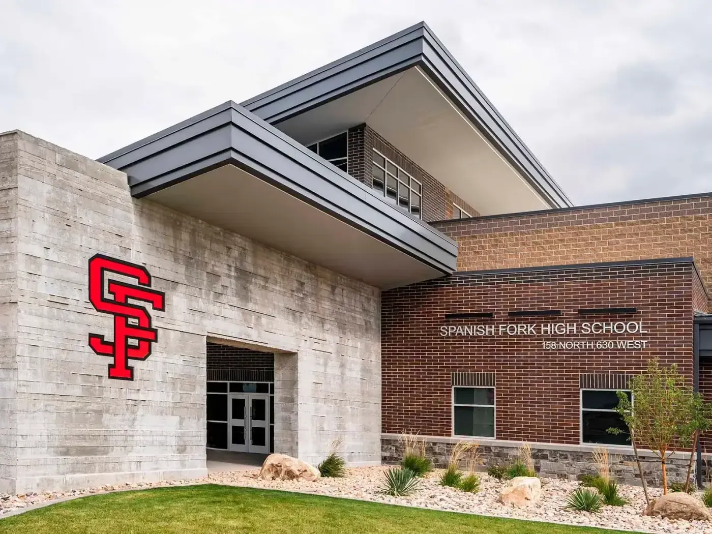 Close-up of the school entrance with the red SF logo, a gray metal canopy, and the Spanish Fork High School sign on a brick wall.