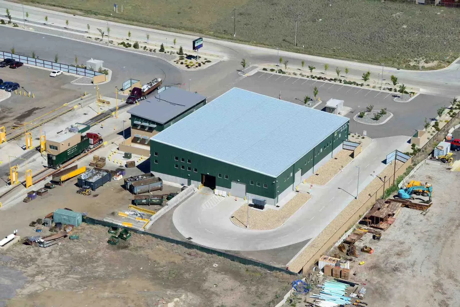 Aerial view of the green warehouse with a light-colored roof, the attached office, and the surrounding yard