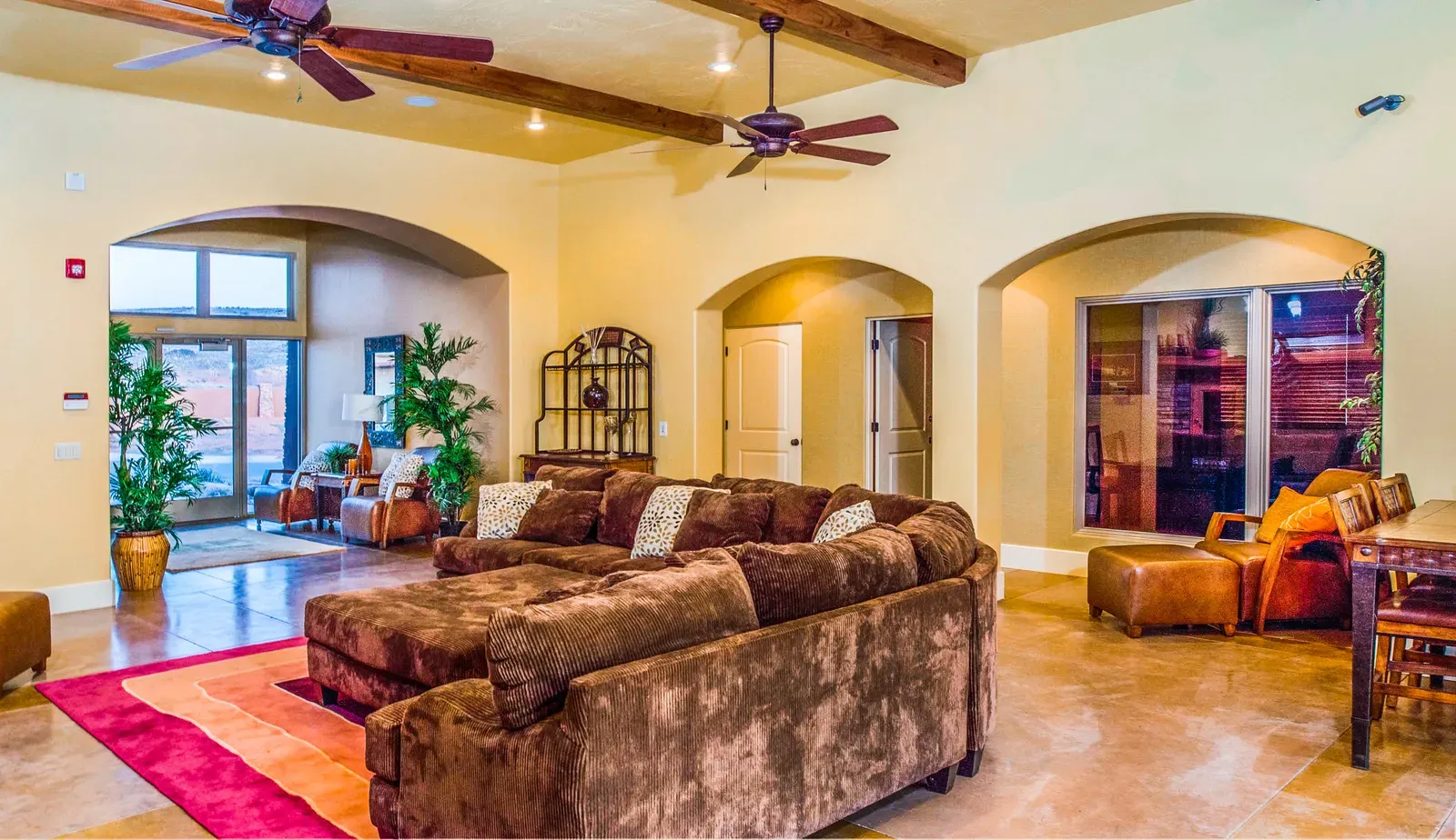 Clubhouse great room with arched openings, exposed wood beams, ceiling fans and a large brown sectional sofa
