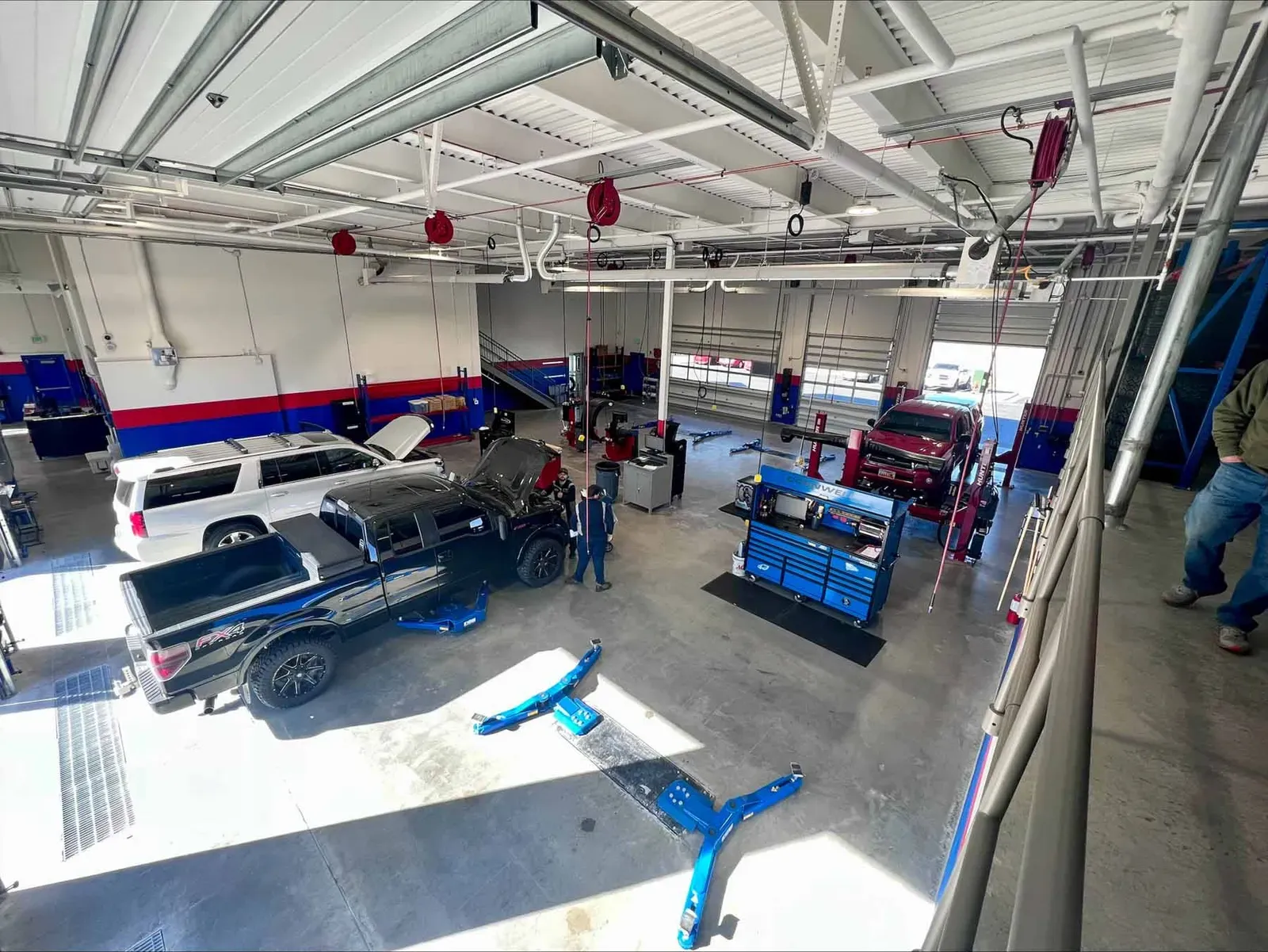 Service shop seen from the mezzanine, with pickup trucks, a mechanic, and blue tire machines