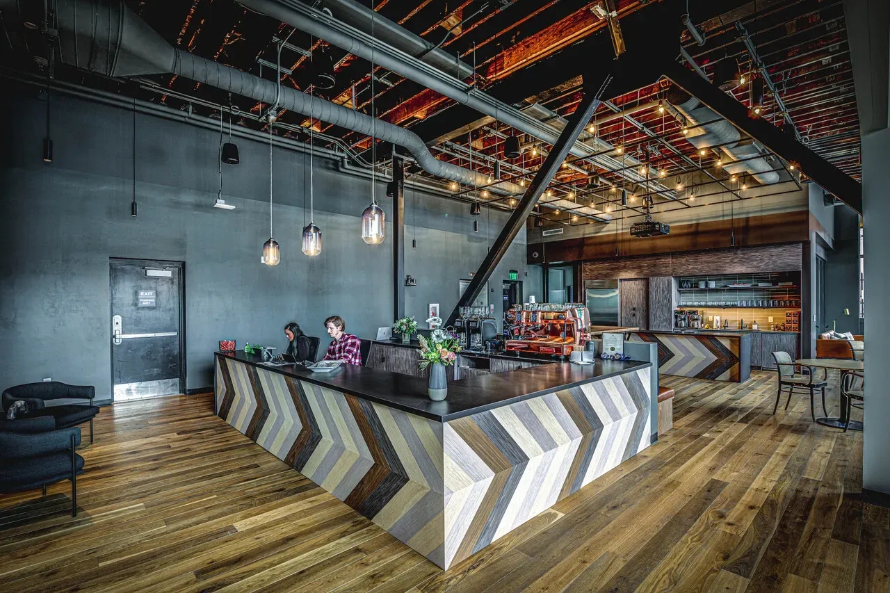 Lounge and coffee bar with a chevron-pattern wood counter, pendant lights and exposed ductwork over wood floors.