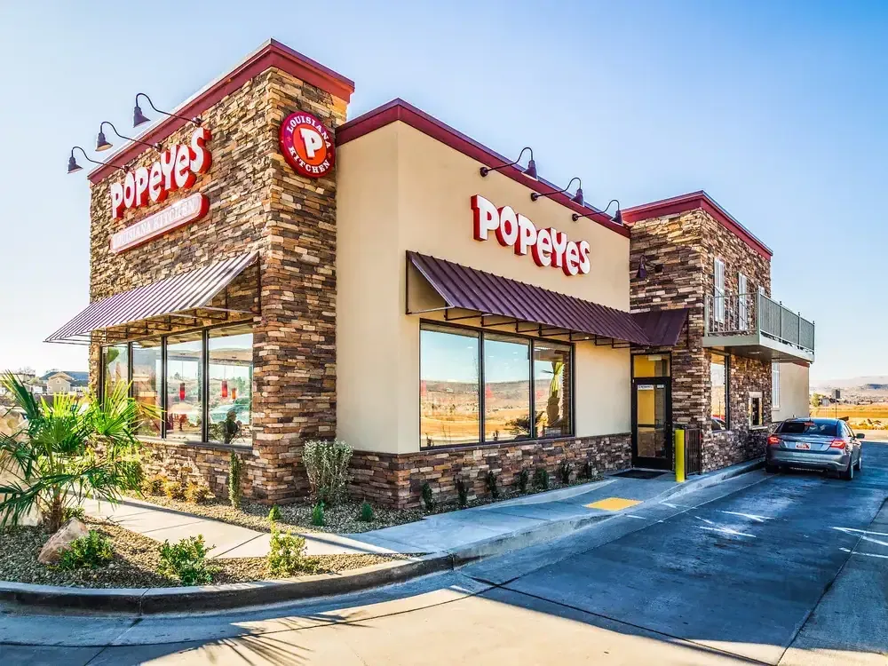 Corner view of the stone and stucco restaurant with red Popeyes signs and the drive-thru lane.