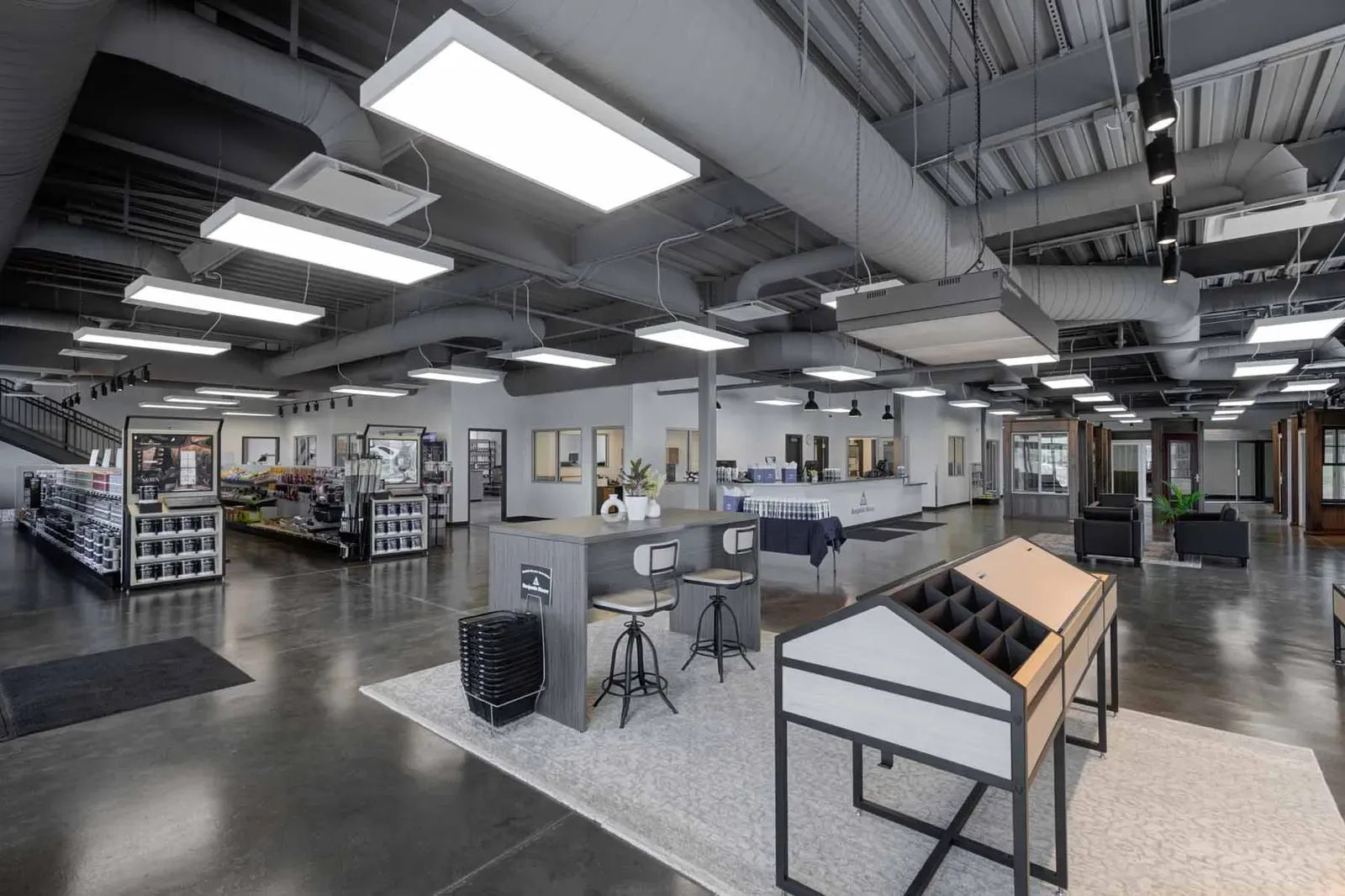 Showroom with a polished concrete floor, exposed ductwork, paint display racks, and a counter with stools