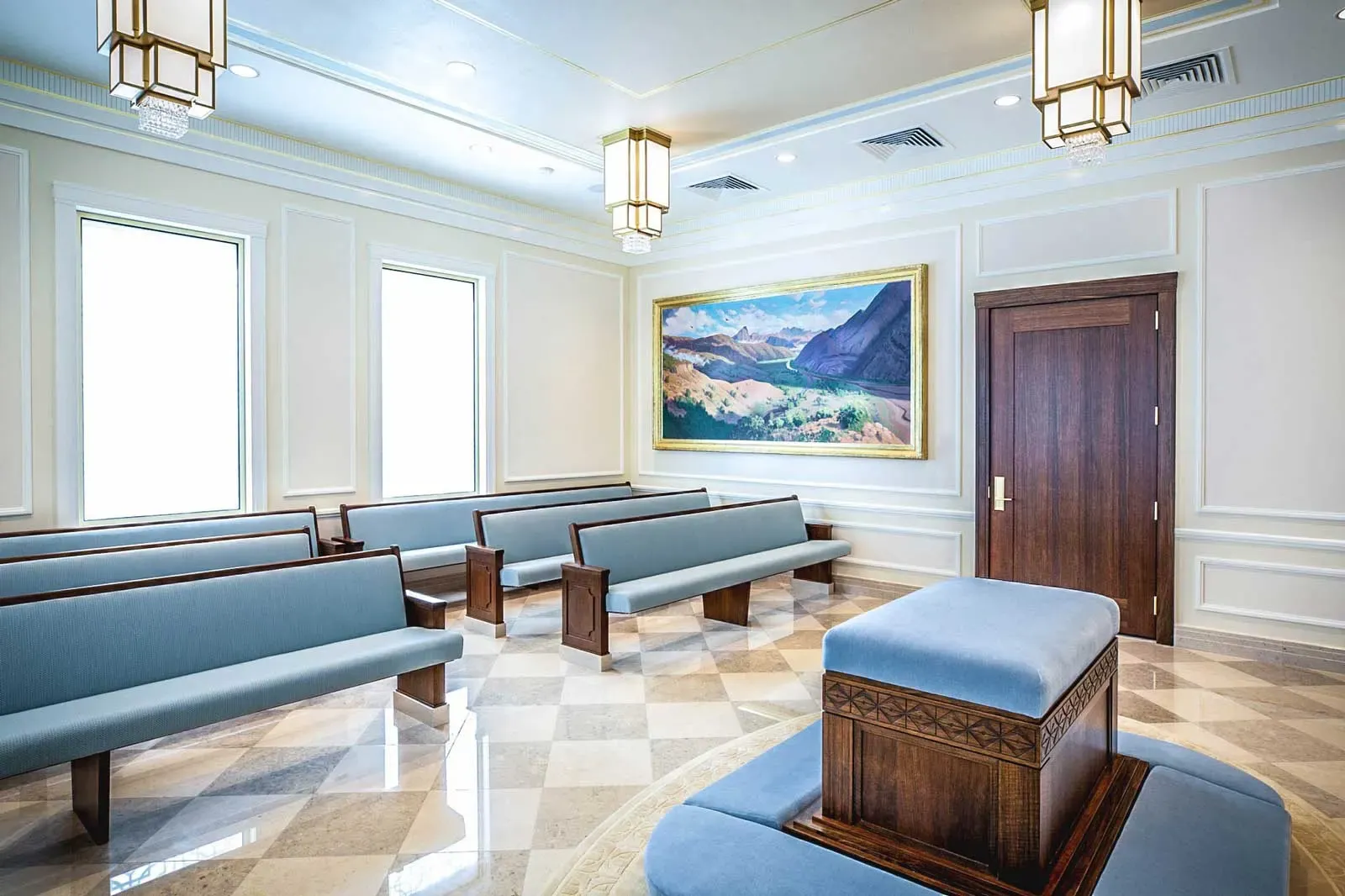 Room with blue-upholstered wooden benches, a landscape painting and a wood door on a patterned marble floor.