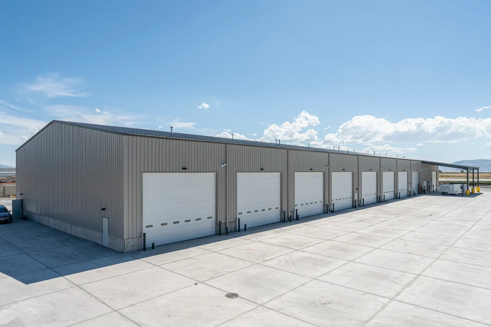 Long gray metal-sided building with a row of white overhead doors on a concrete apron.