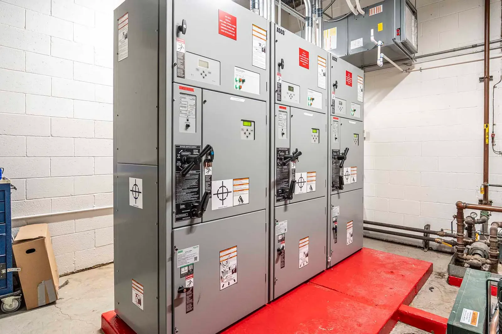 Gray electrical switchgear cabinets on a red base in a block-walled equipment room.