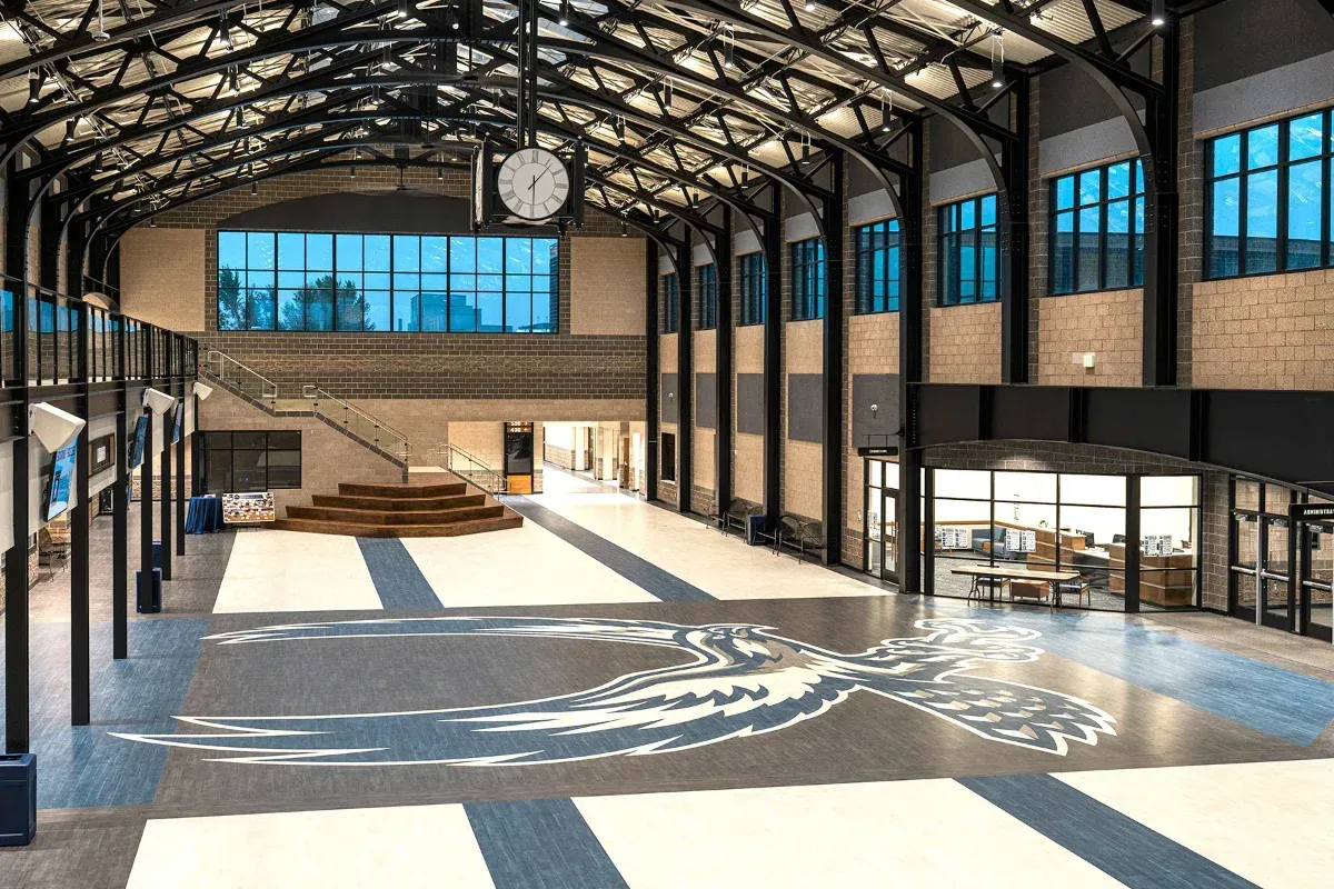 Commons with exposed black steel trusses, a large clock, and a bird emblem inlaid in the floor