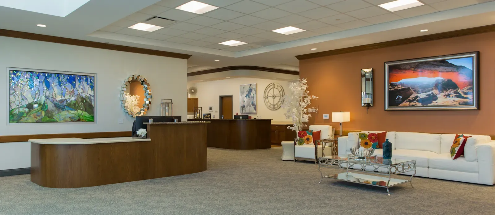 Wide lobby with a curved reception desk, an orange accent wall, and a white sofa seating area.
