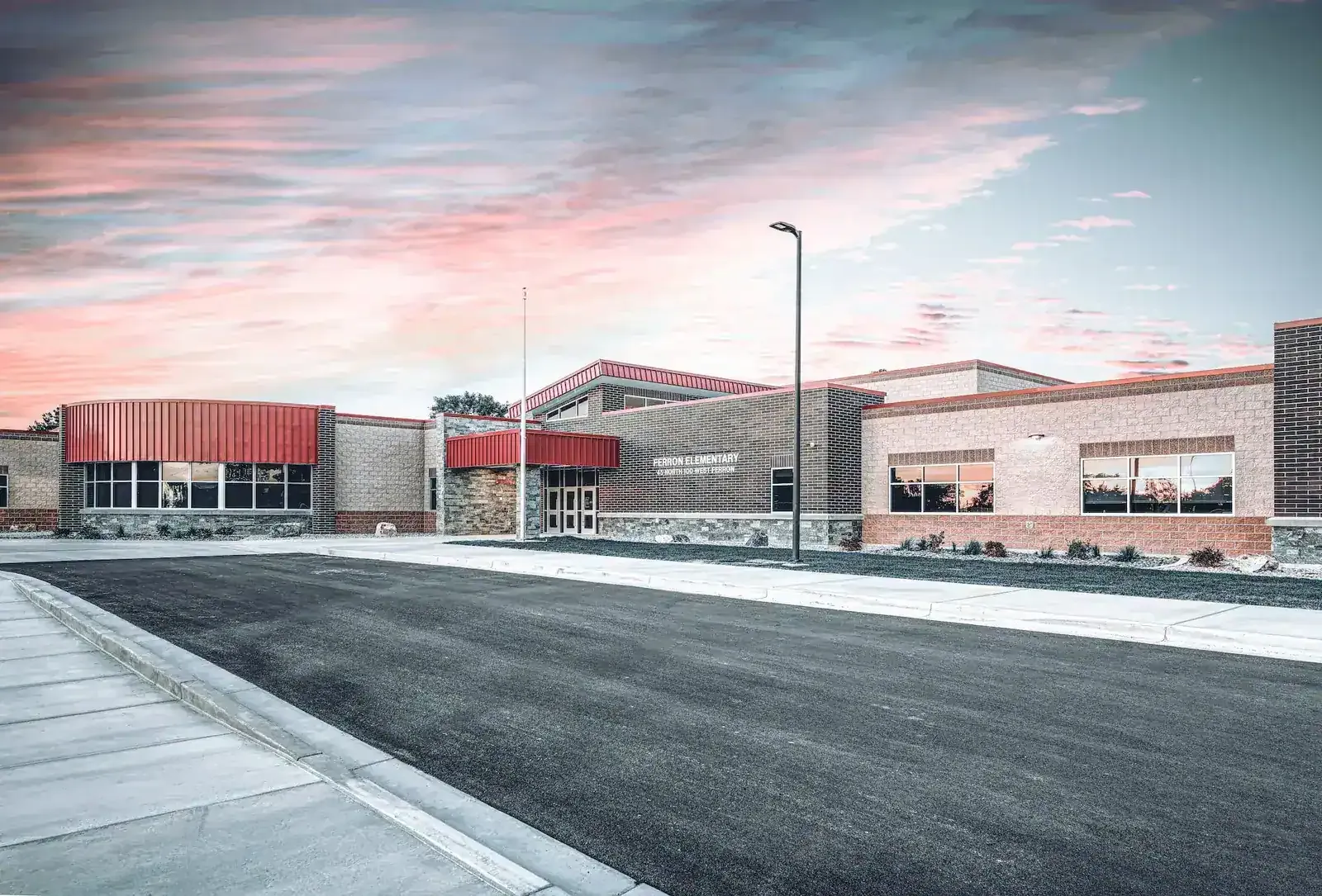 Long brick and stone front of the school with red metal accents under a pink dusk sky