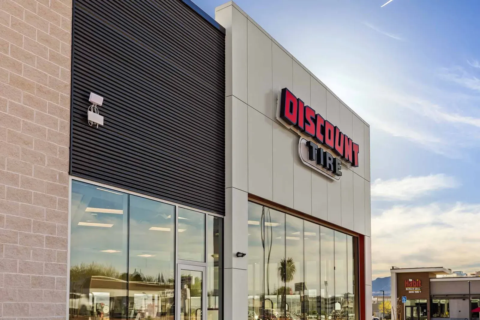 Red Discount Tire sign on a light panel wall beside a tall glass storefront