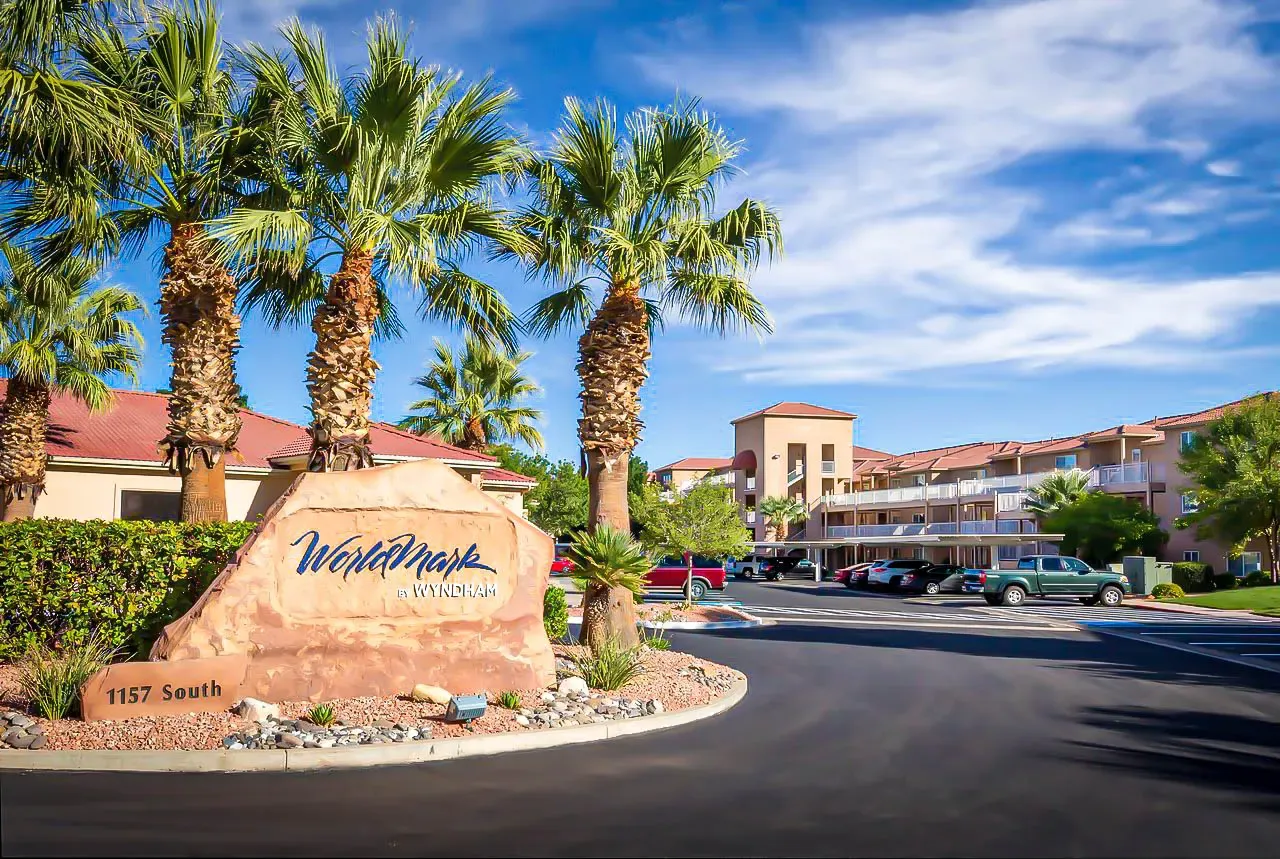 Resort entrance drive with a red sandstone sign reading WorldMark by Wyndham, palm trees and a multi-story stucco building beyond