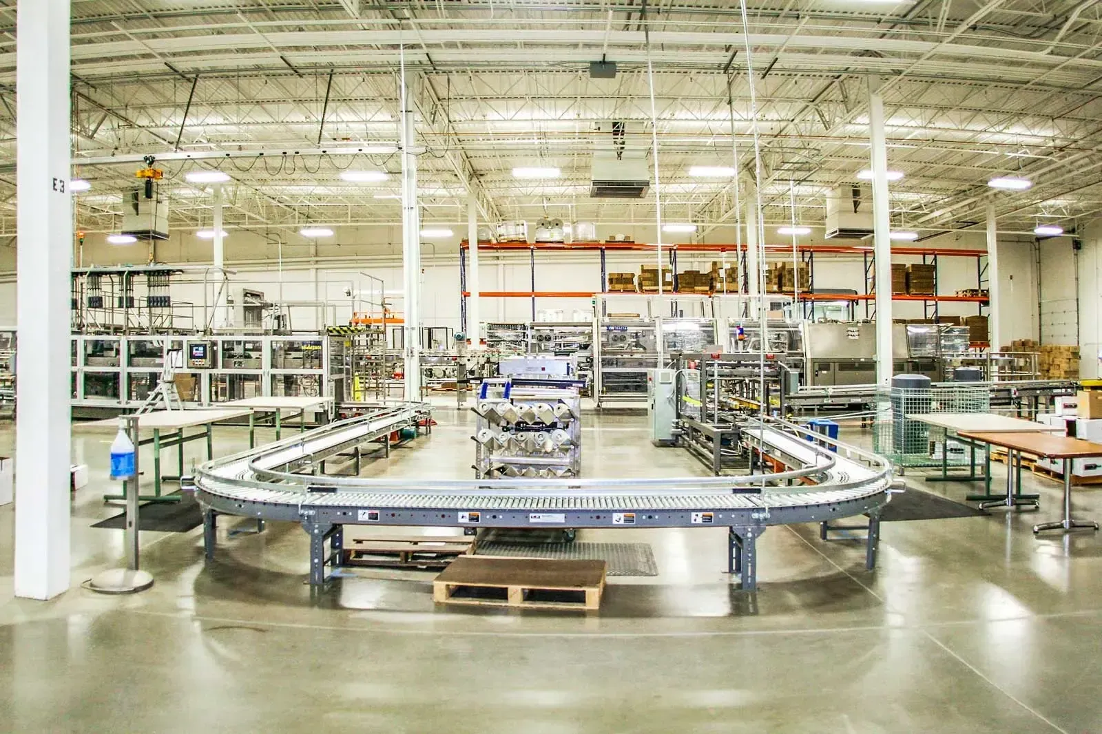 Production floor with a curved conveyor and packaging equipment under a high steel roof.