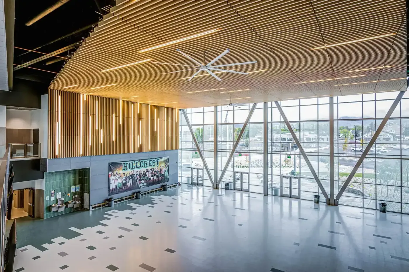 Main lobby with a curved wood-slat ceiling, a tall angled glass wall and a Hillcrest banner of students